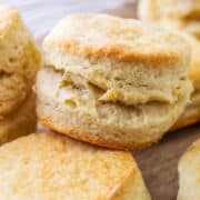 Golden, flaky biscuits stacked on wood, highlighting their airy texture and crisp edges.