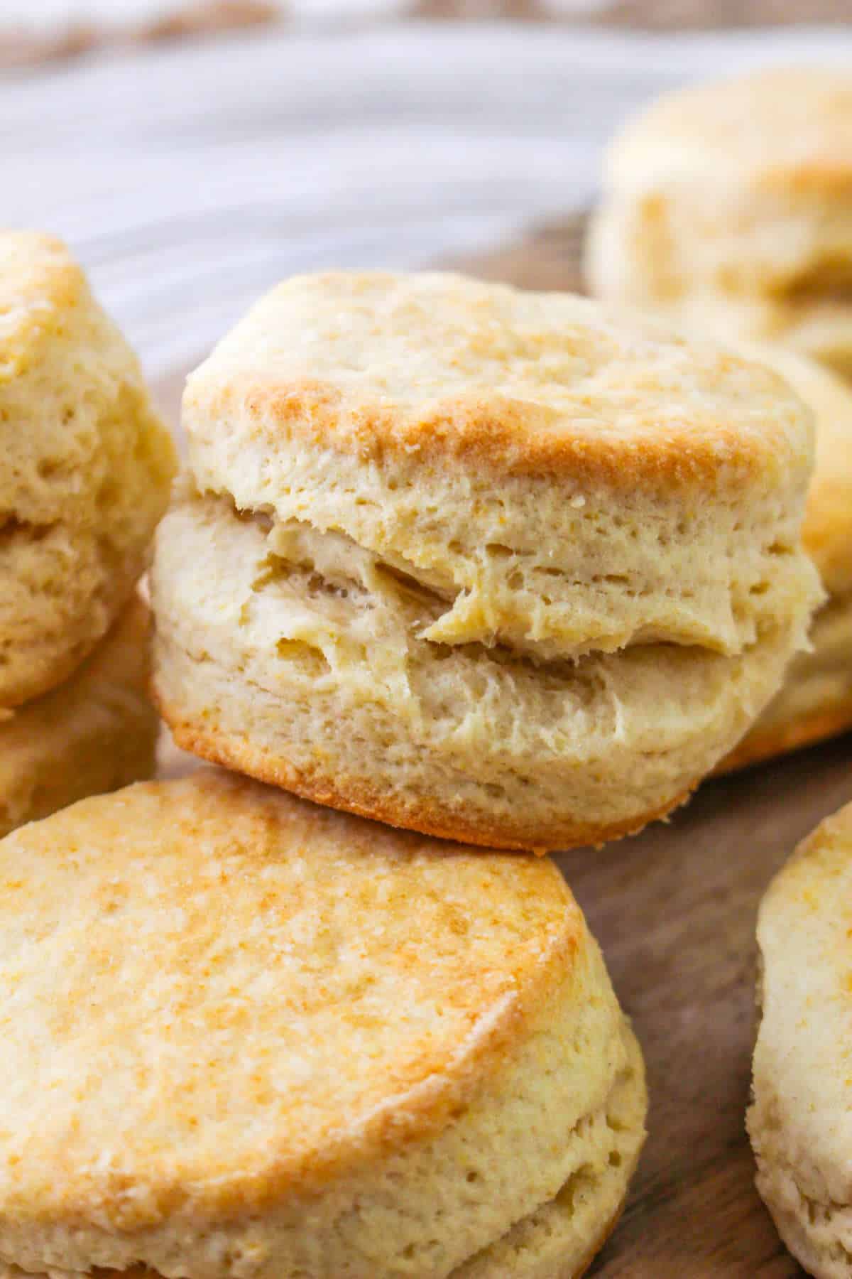 Golden, flaky biscuits stacked on wood, highlighting their airy texture and crisp edges.