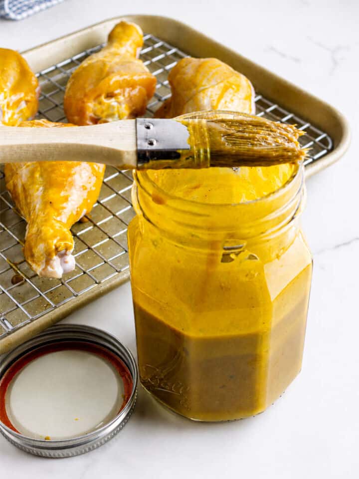 Carolina Gold BBQ sauce in an open jar beside sauced chicken drumsticks on a wire rack.