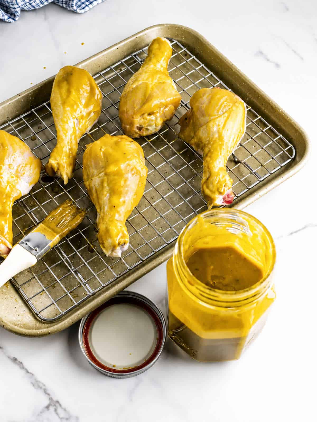 Chicken drumsticks brushed with Carolina Gold BBQ sauce on a wire rack with a jar of sauce nearby.