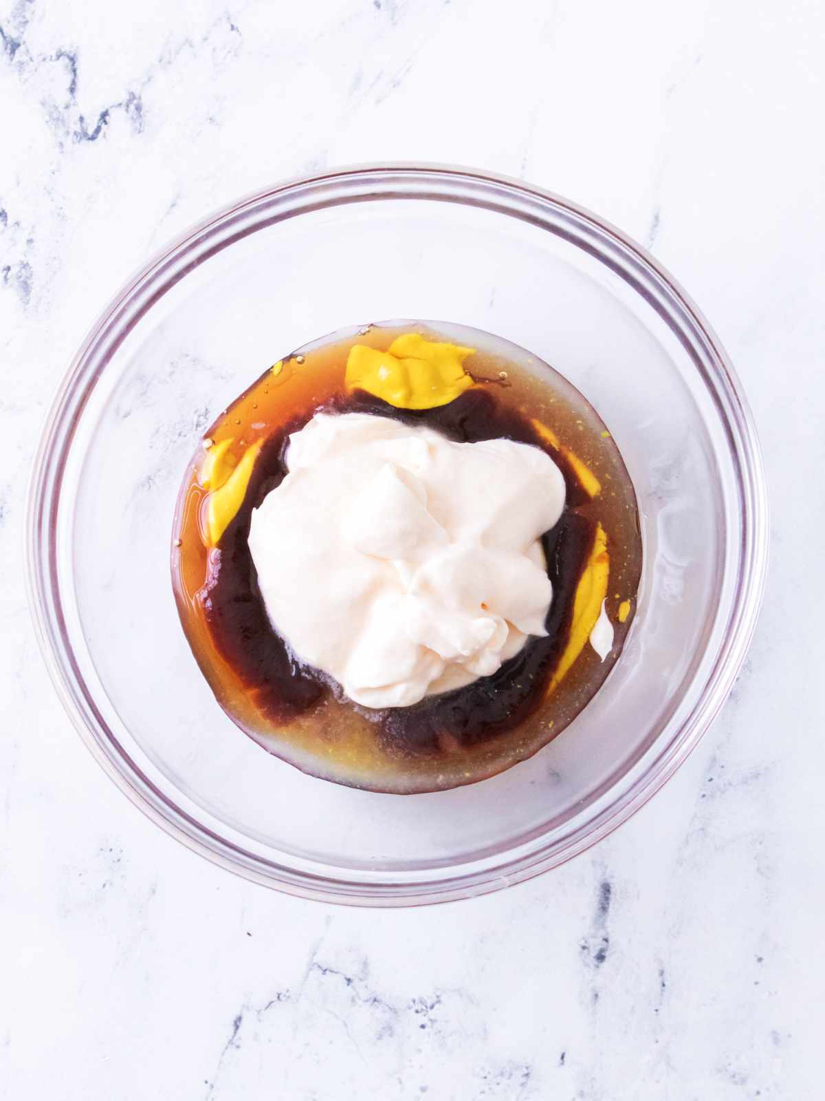 Glass bowl with mayonnaise, mustard, ketchup, and Worcestershire sauce on white marble before mixing.