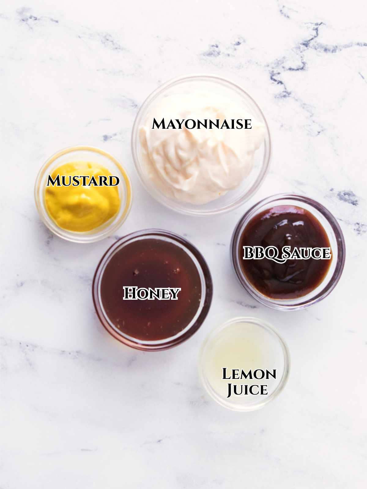 Five glass bowls with mayonnaise, BBQ sauce, mustard, honey, and lemon juice sit on white marble, each labeled.
