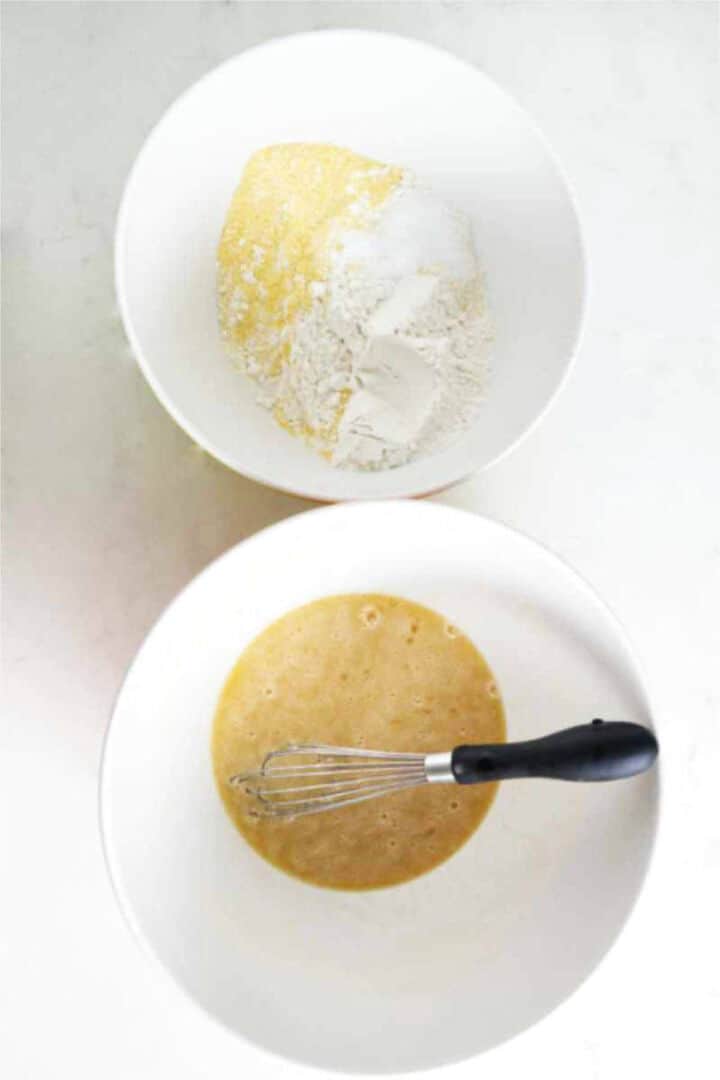 Two mixing bowls with dry ingredients and whisked wet ingredients for cornbread muffins.