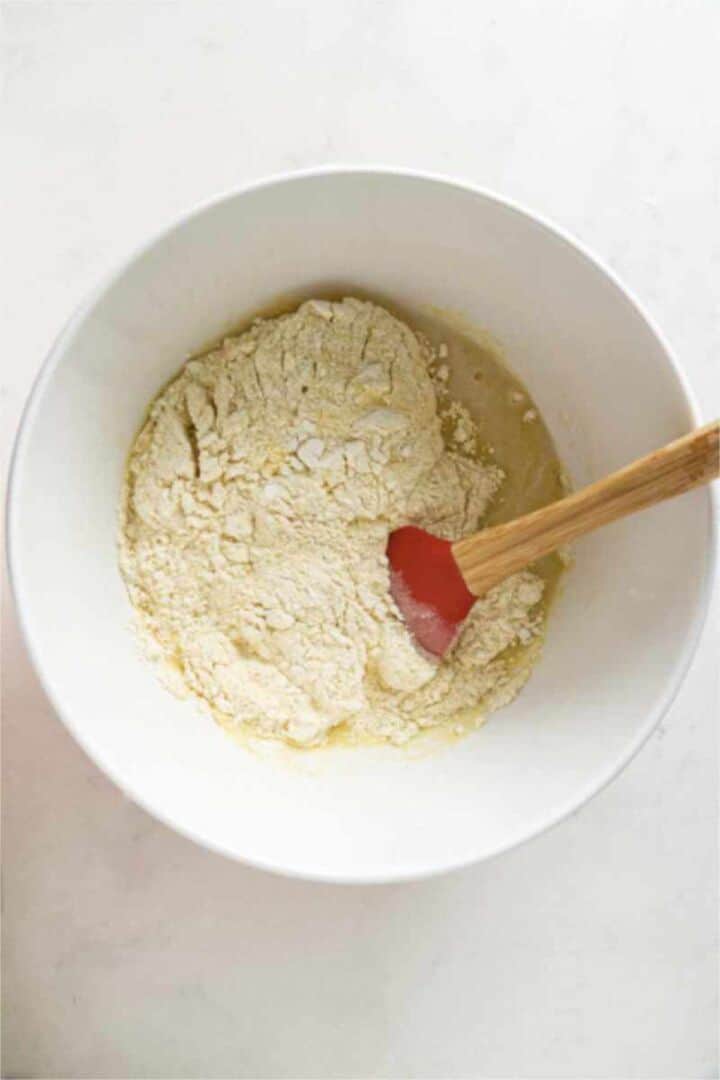 Cornbread muffin batter mixed in a white bowl with a red silicone spatula.