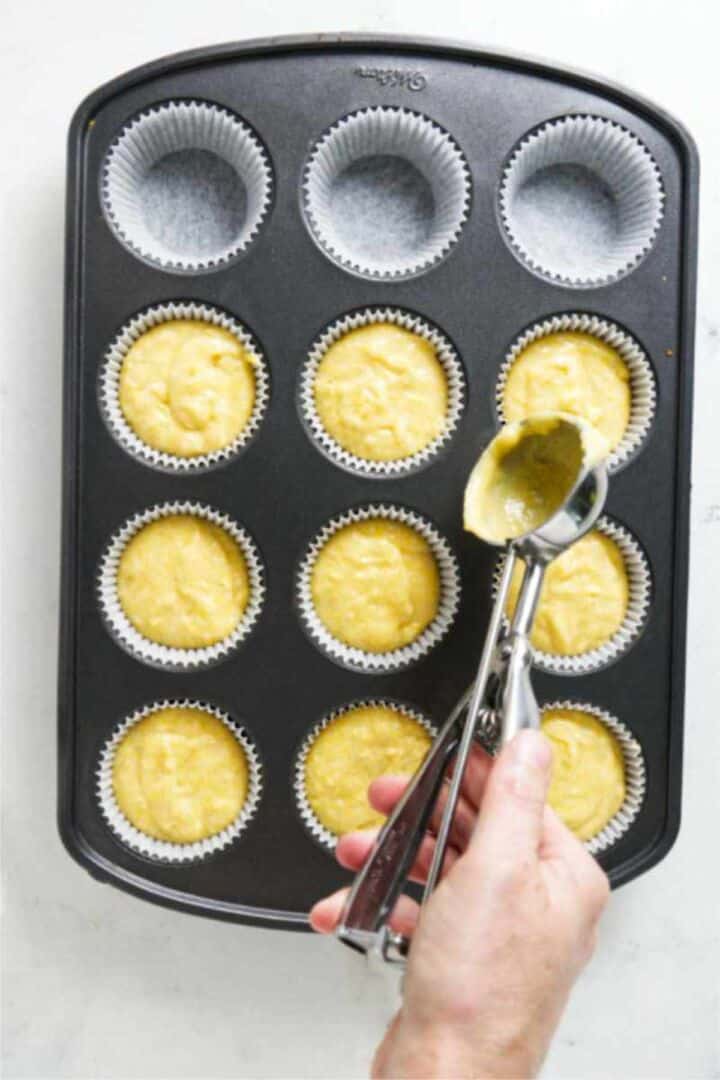 Cornbread muffin batter being scooped into a paper-lined muffin pan.