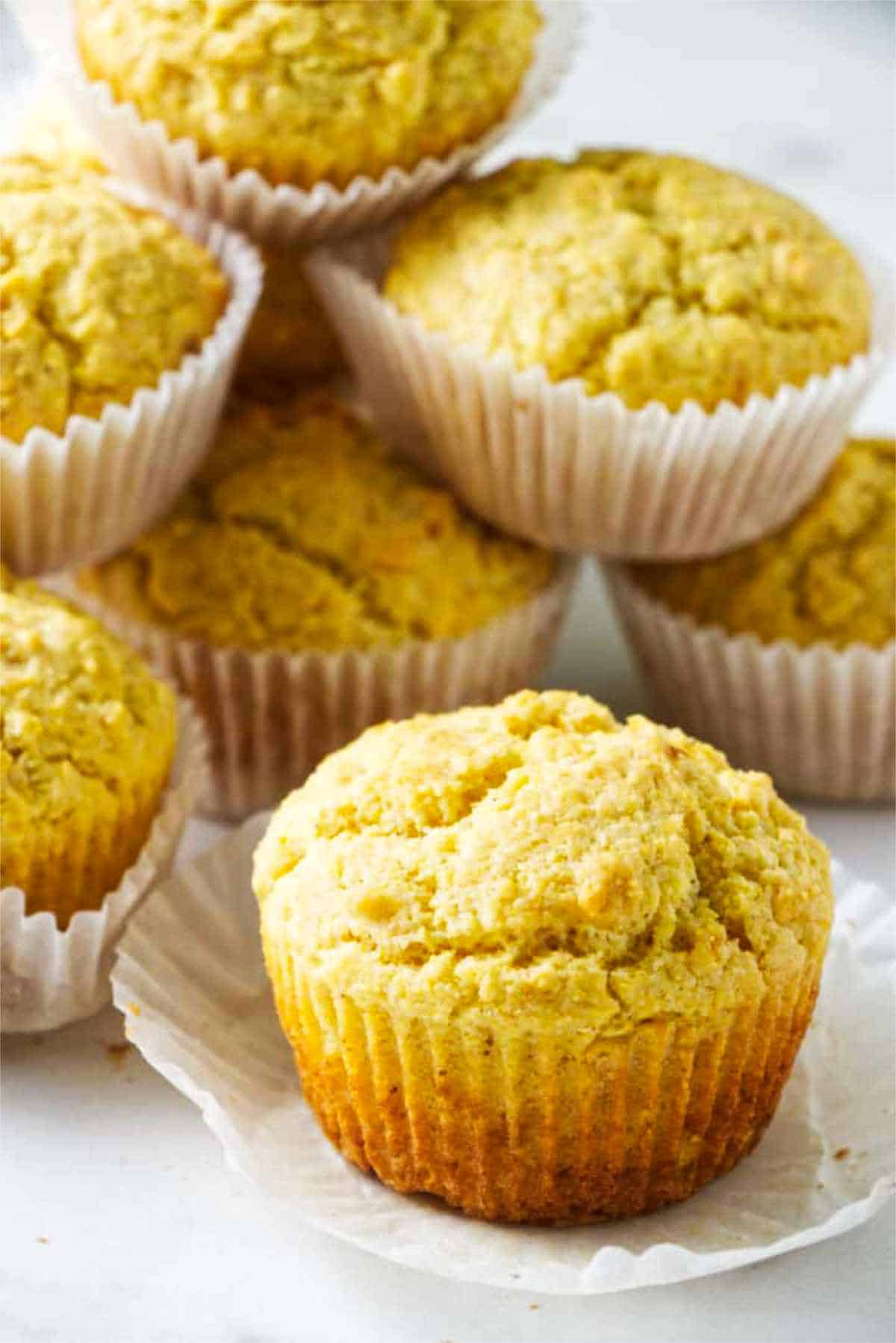 Close-up of golden cornbread muffins in white liners with one unwrapped in front.