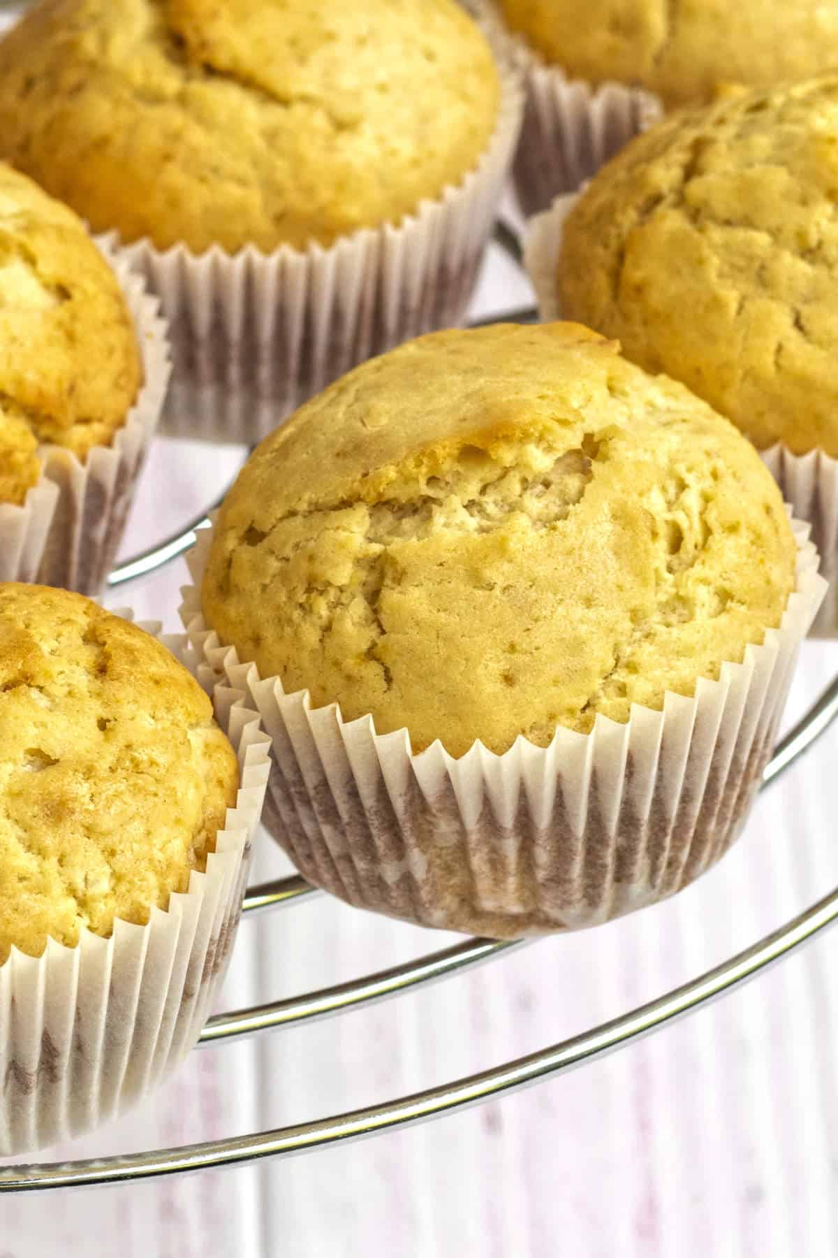 Freshly baked cornbread muffins cooling in white paper liners on a round wire rack.