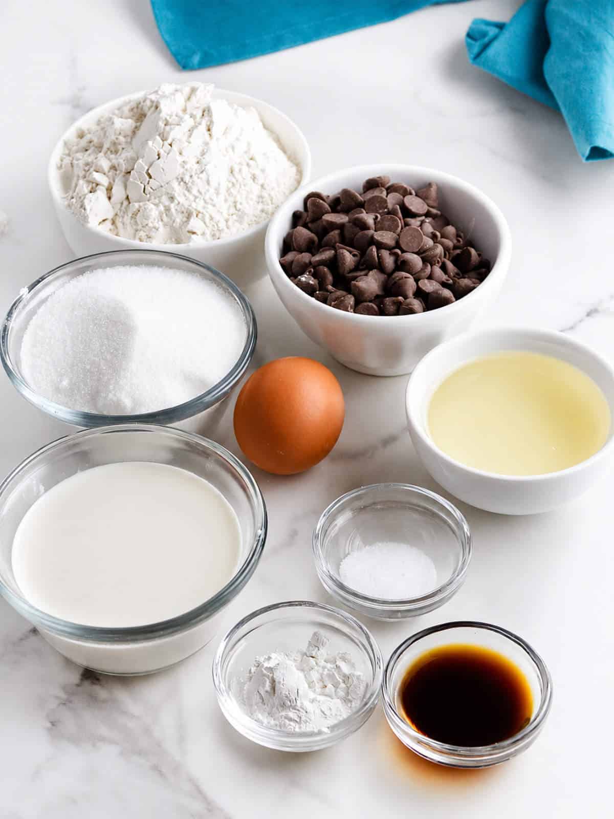 Ingredients for gluten free chocolate chip muffins with 1:1 gluten free flour, chocolate chips, sugar, milk, oil, egg, vanilla, baking powder, and salt.