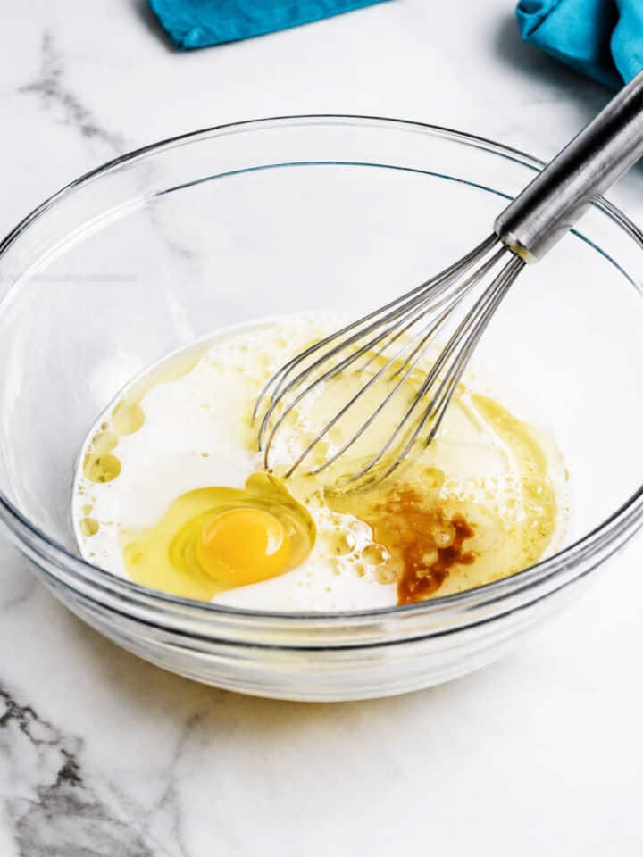 Milk, egg, vegetable oil, and vanilla in a glass bowl with a whisk for gluten free chocolate chip muffins.
