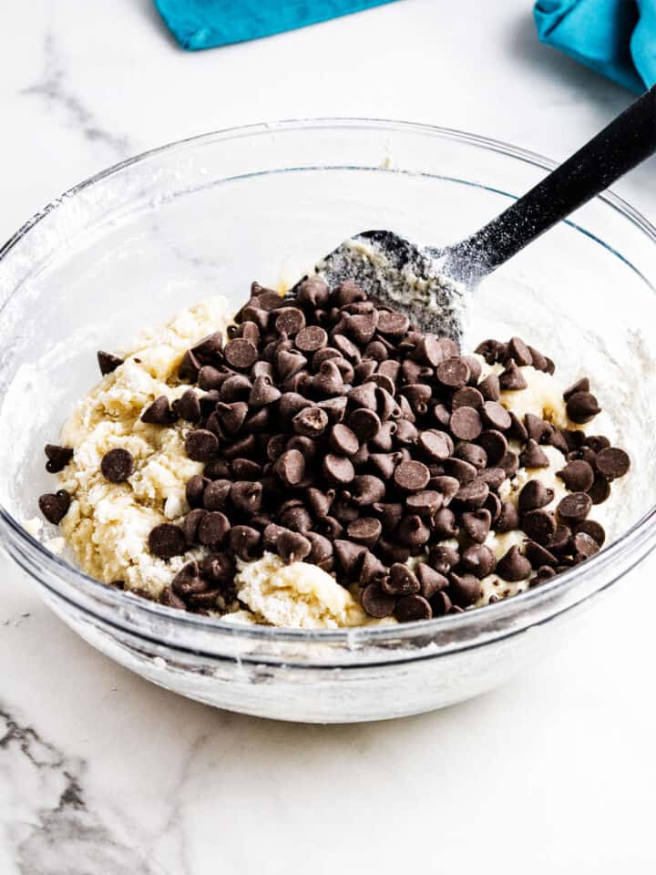 Gluten free chocolate chip muffin batter mixed in a glass bowl on a white marble surface.