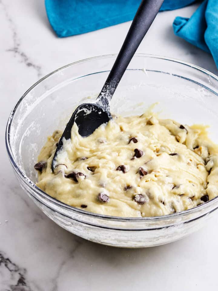 Chocolate chips folded into gluten free muffin batter in a glass bowl with a black spatula.
