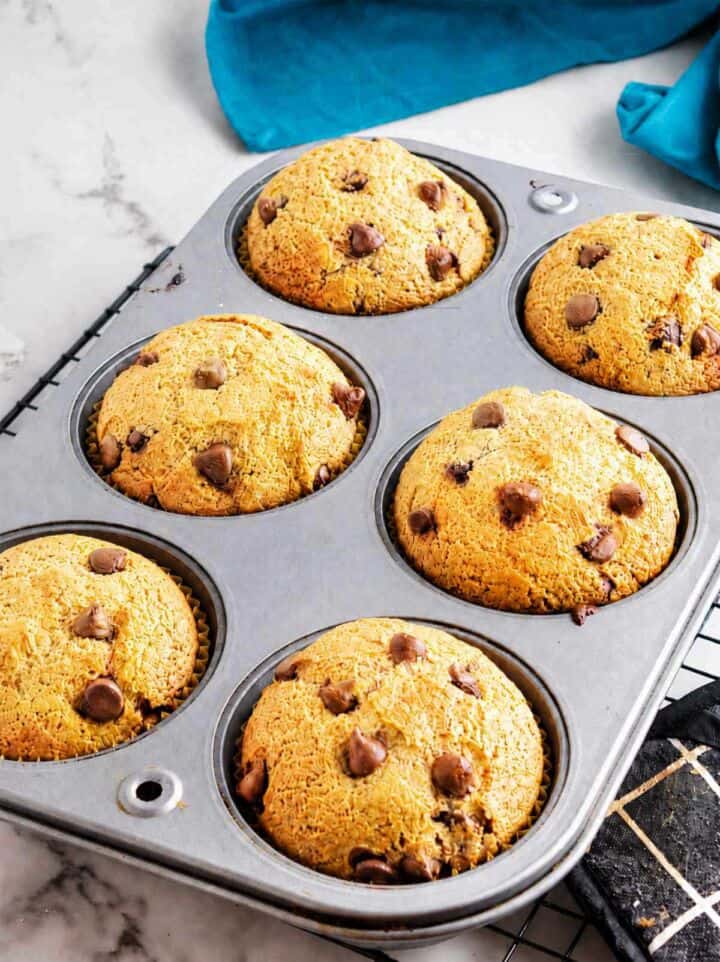 Baked gluten free chocolate chip muffins in a muffin pan cooling on a wire rack.