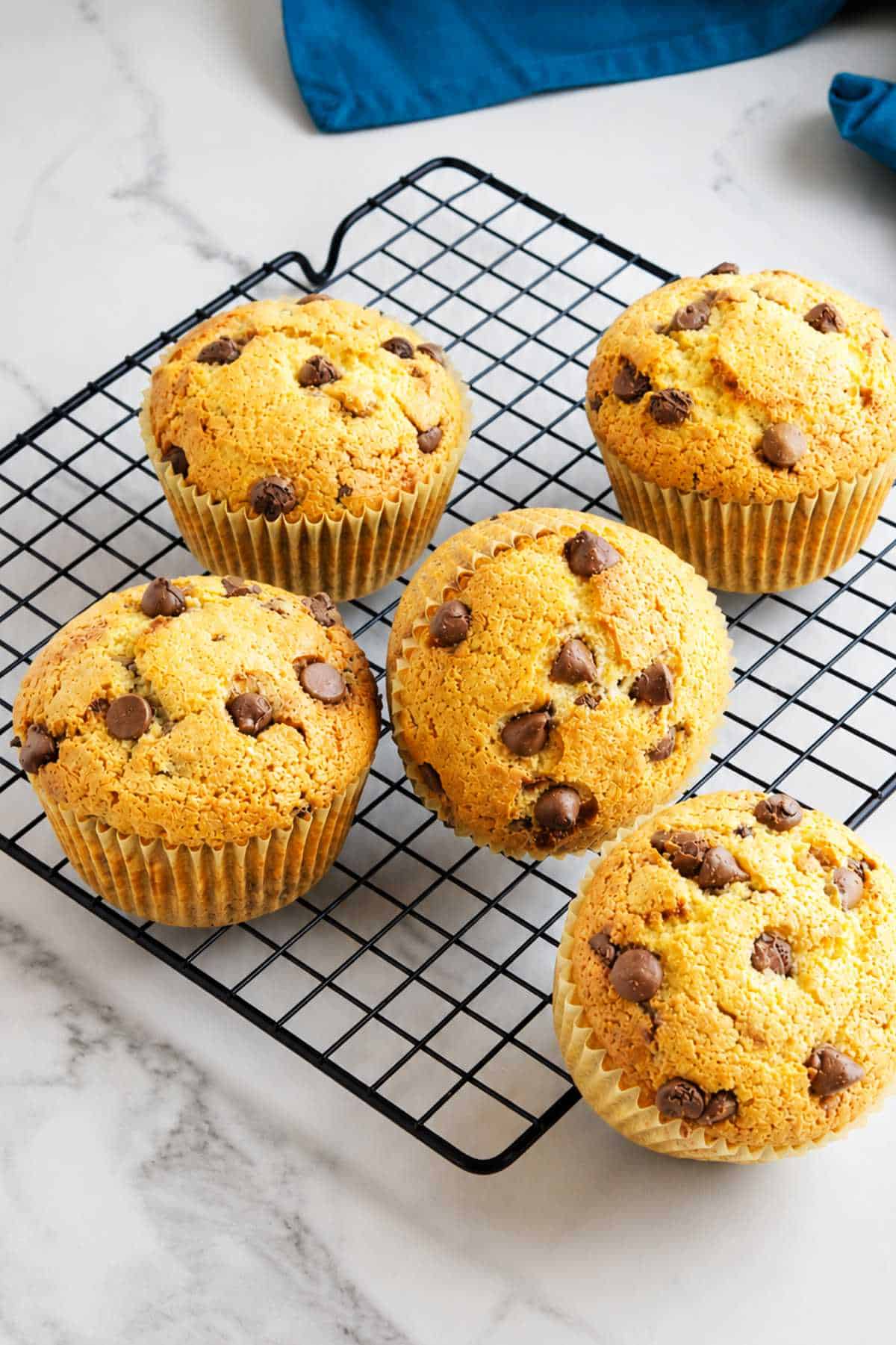 Baked gluten free chocolate chip muffins cooling on a black wire rack over white marble.