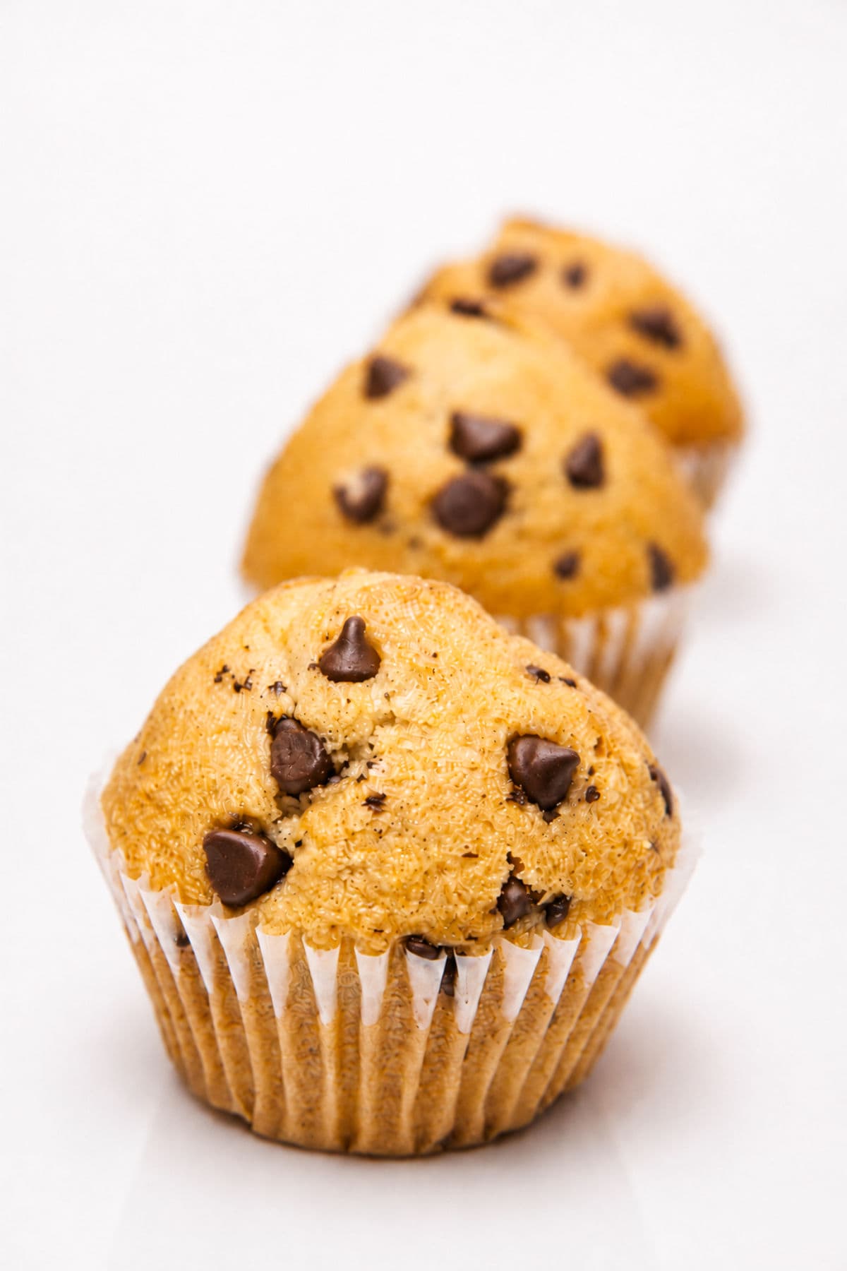 Tall gluten free chocolate chip muffins with golden domes and chocolate chips on a white background.