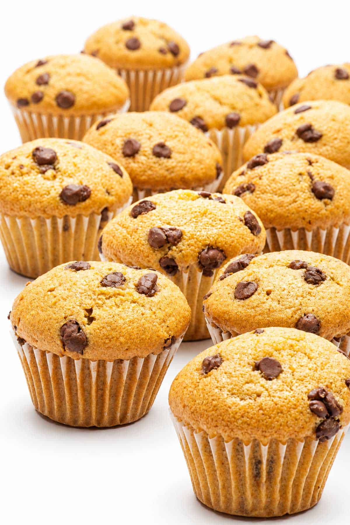 Gluten free chocolate chip muffins with golden tops and chocolate chips grouped on a white surface.