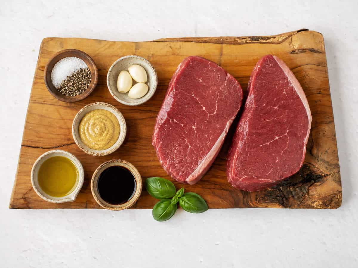 Two raw top sirloin steaks with balsamic vinegar, olive oil, Dijon mustard, garlic, basil, salt, and pepper.