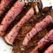 Medium-rare grilled top sirloin slices on a white plate with herbs, and olive oil.