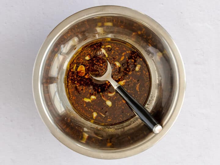 Balsamic steak marinade with Dijon mustard, olive oil, garlic, basil, salt, and pepper in a metal bowl.