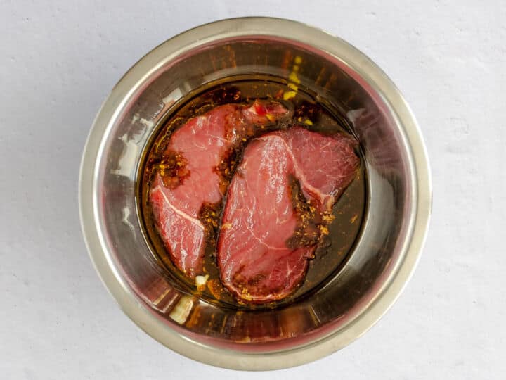 Raw top sirloin steaks added to a bowl of balsamic marinade.