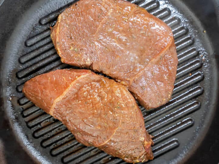 Marinated top sirloin steaks placed on a hot cast iron grill pan.