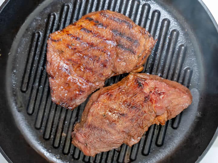 Two grilled top sirloin steaks with sear marks on a cast iron grill pan.