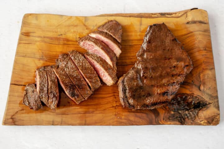 Grilled top sirloin steak resting on a wooden board with one steak sliced to show a pink center.