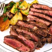 Grilled sirloin slices with golden roasted potatoes and fresh herbs neatly arranged on a plate, showing juicy meat and crisp potatoes.