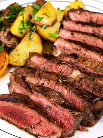 Grilled sirloin slices with golden roasted potatoes and fresh herbs neatly arranged on a plate, showing juicy meat and crisp potatoes.