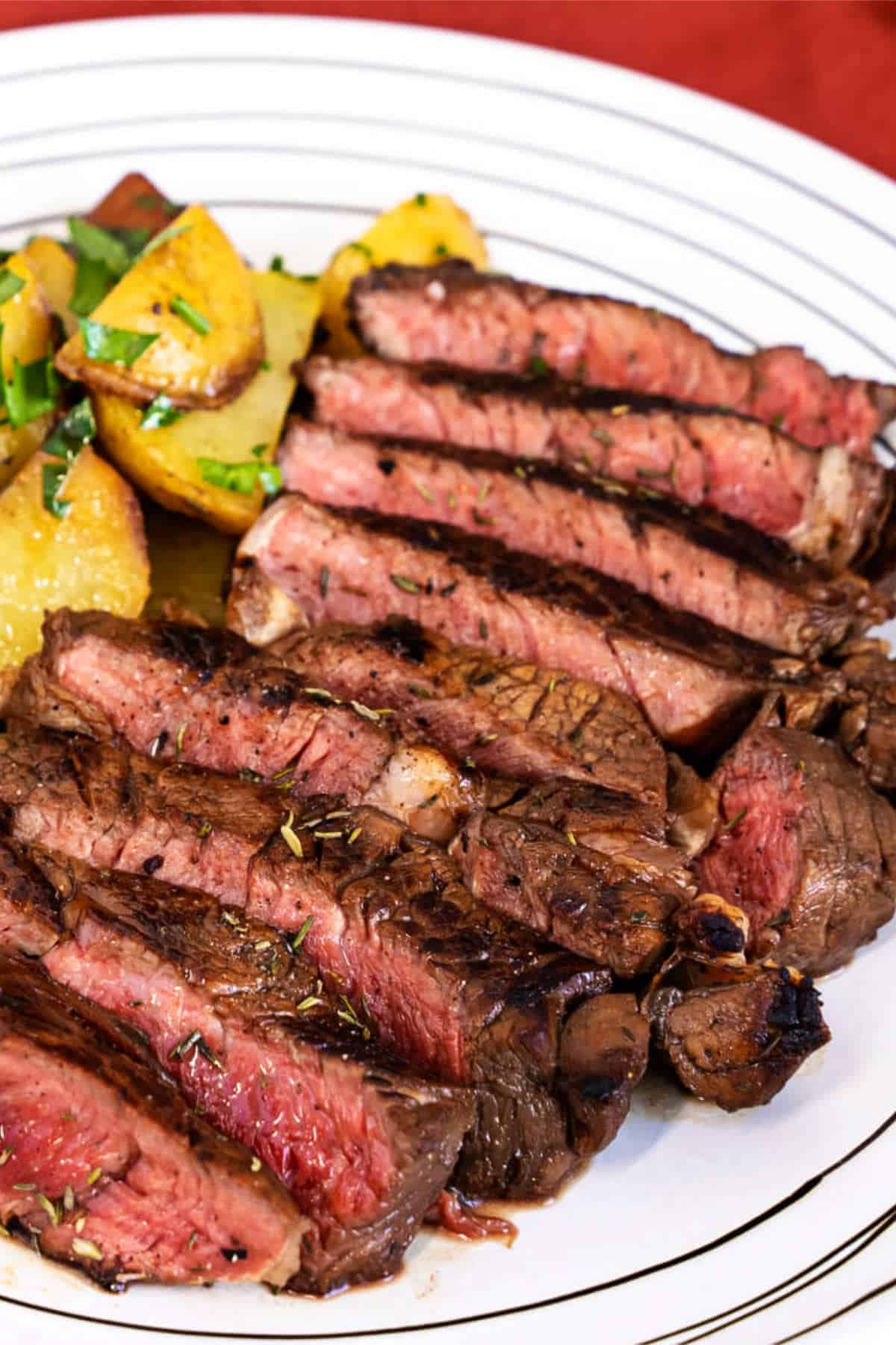 Grilled top sirloin steak slices served with roasted potatoes and fresh herbs on a white plate.