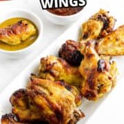 Plate of honey gold chicken wings with honey gold and barbecue sauces on a white surface.