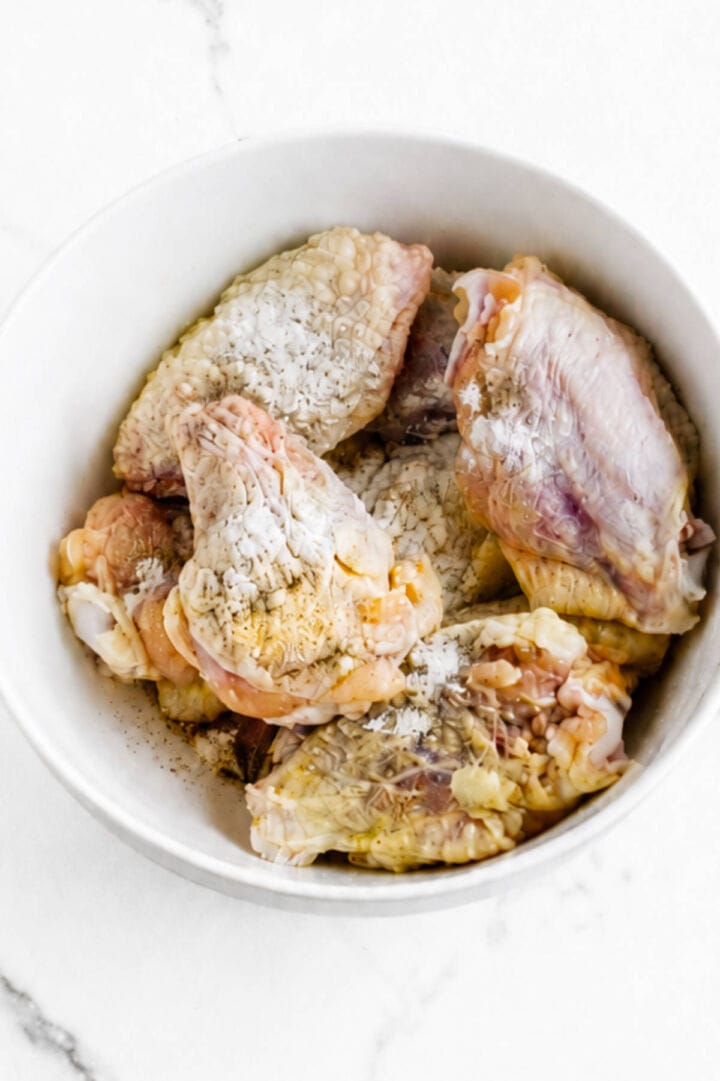 Chicken wings in a white bowl coated with baking powder and seasonings before baking.