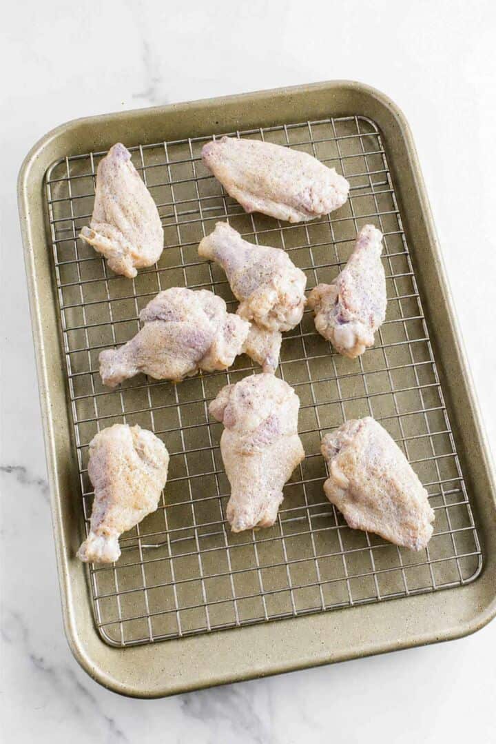 Seasoned chicken wings arranged on a wire rack over a baking sheet before baking.