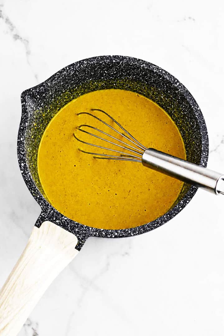 Golden Honey Gold BBQ sauce simmering in a saucepan with a whisk.