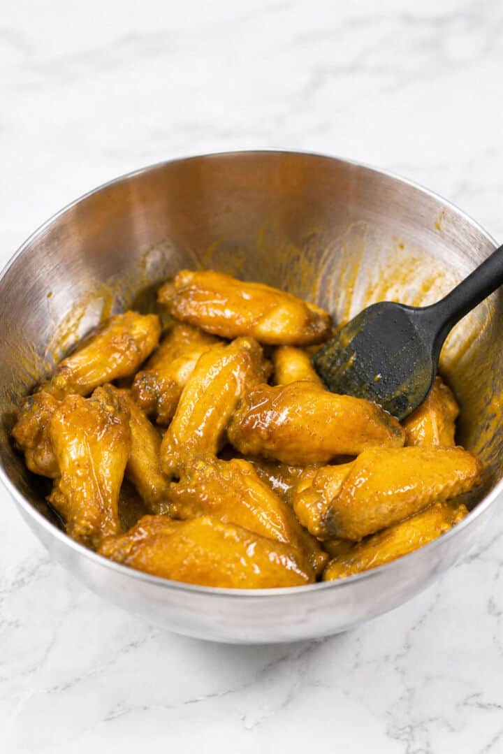 Baked chicken wings tossed with Honey Gold BBQ sauce in a metal mixing bowl.
