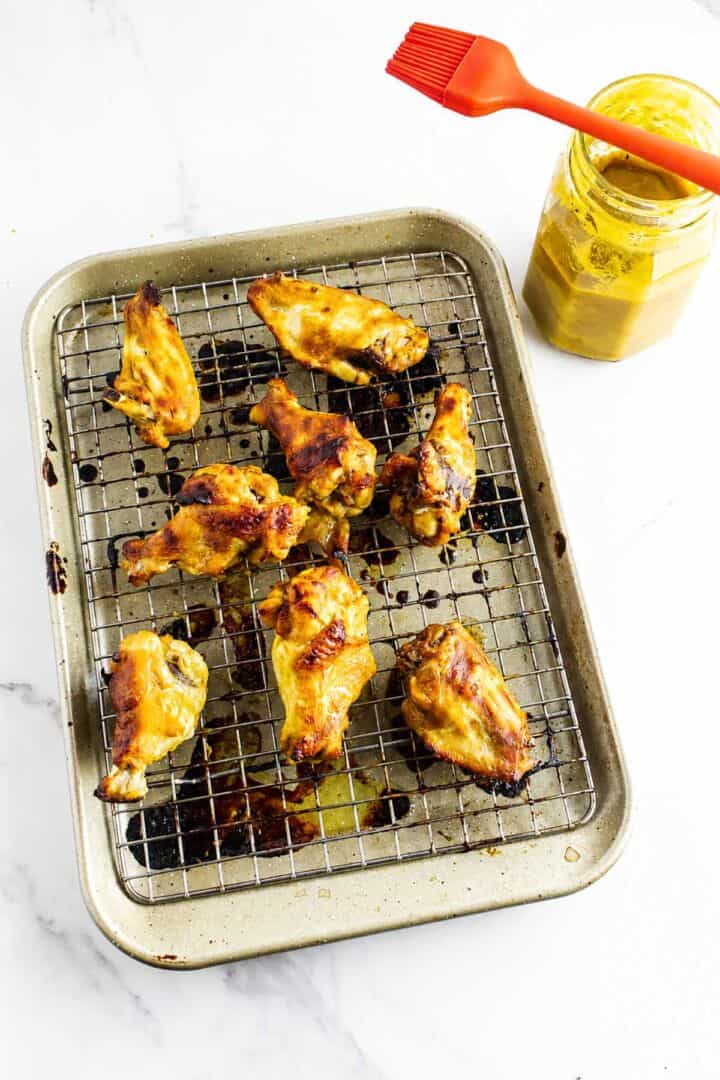 Sauced Honey Gold Wings on a wire rack with a jar of golden BBQ sauce and a basting brush.