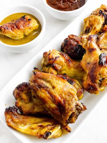 White plate of golden-brown Honey Gold chicken wings with mustard and barbecue sauces, set on a white surface.