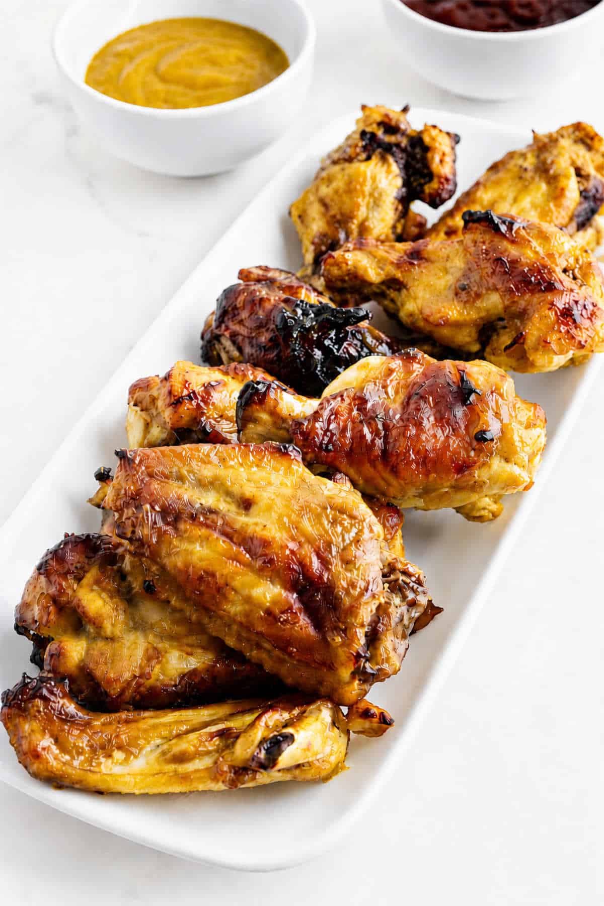 Platter of Honey Gold Wings with golden BBQ glaze and dipping sauces in the background.