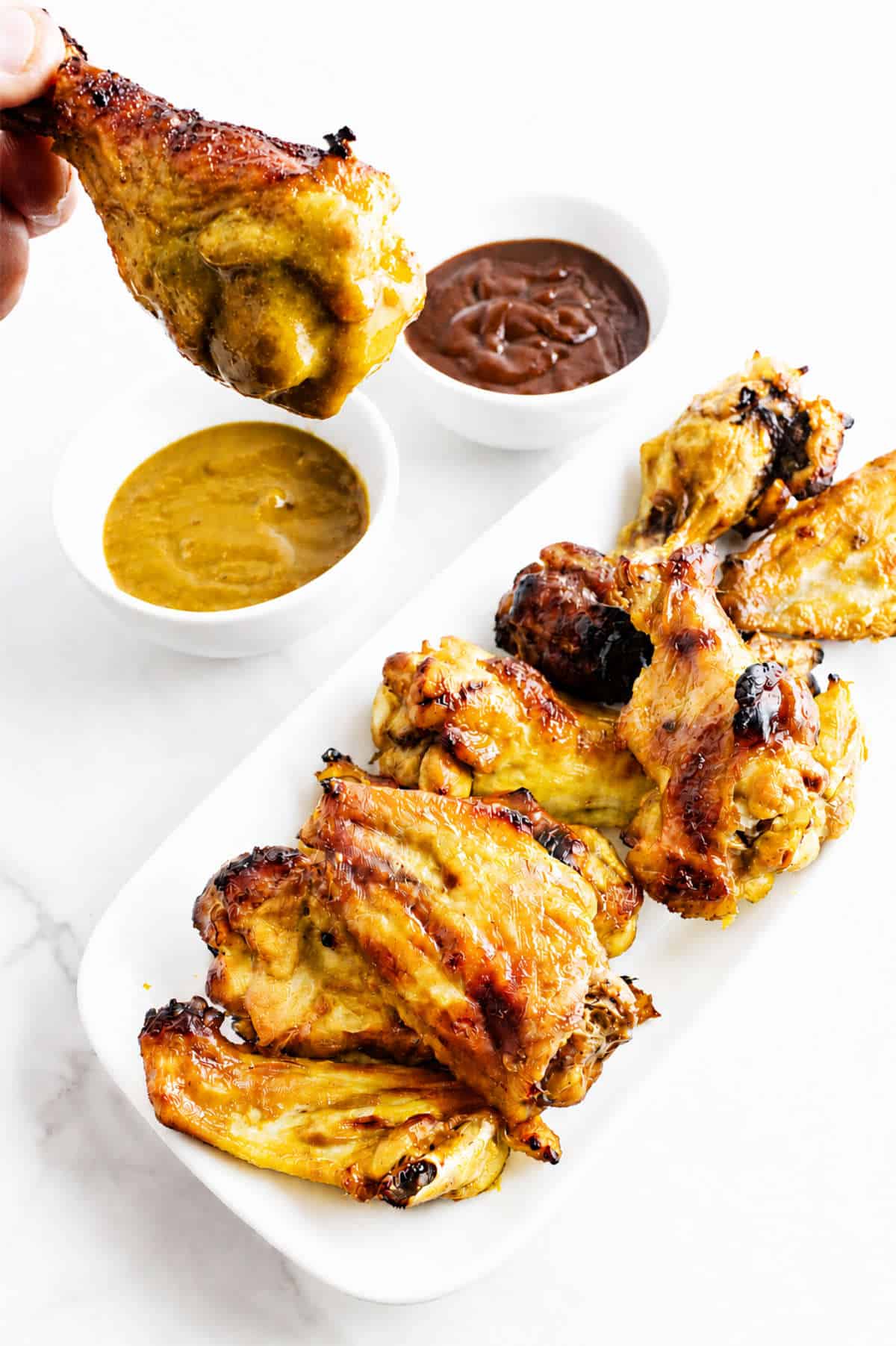 Honey Gold chicken wings with glossy golden BBQ sauce and a hand holding one wing over the platter.