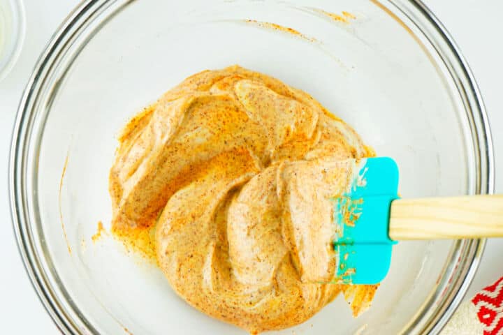 Chipotle mayonnaise in a glass bowl being stirred with a blue spatula for a Panera Chipotle Chicken Avocado Melt.