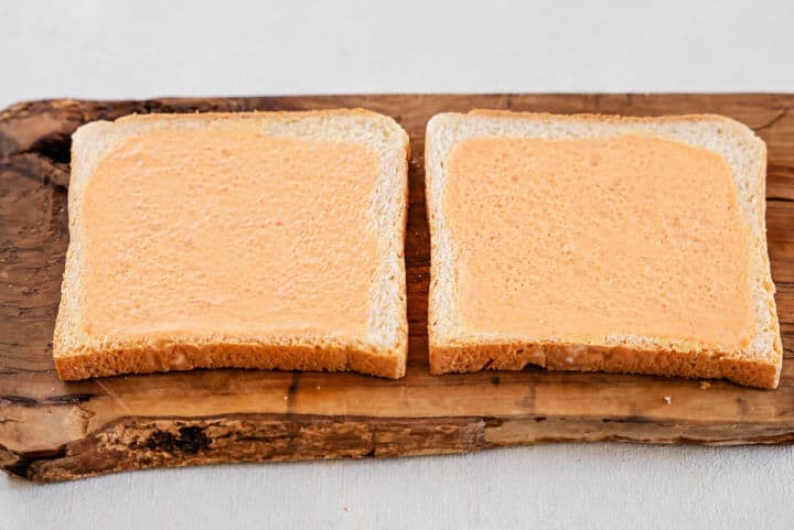 Two slices of bread spread with orange chipotle mayo on a rustic wooden board for Panera chicken avocado melts.