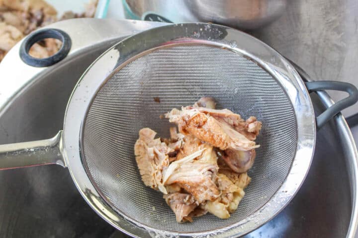 Cooked chicken pieces strained in a metal sieve while making broth for chicken noodle soup.