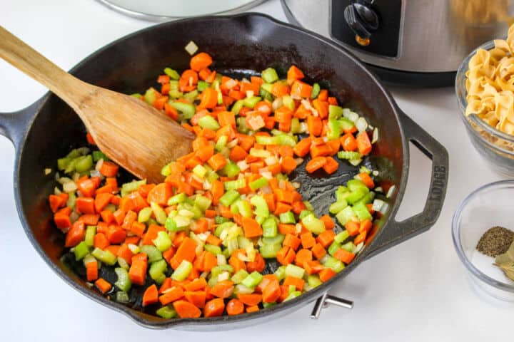 Carrots, celery, and onion sautéing in a skillet for slow cooker chicken noodle soup.