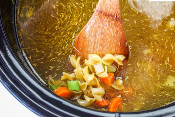 Egg noodles cooking with chicken, vegetables, and broth in a slow cooker.