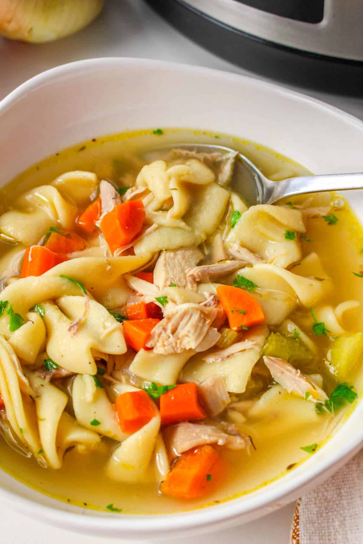 Panera chicken noodle soup recipe served in a bowl with broth, noodles, chicken, vegetables, and herbs.