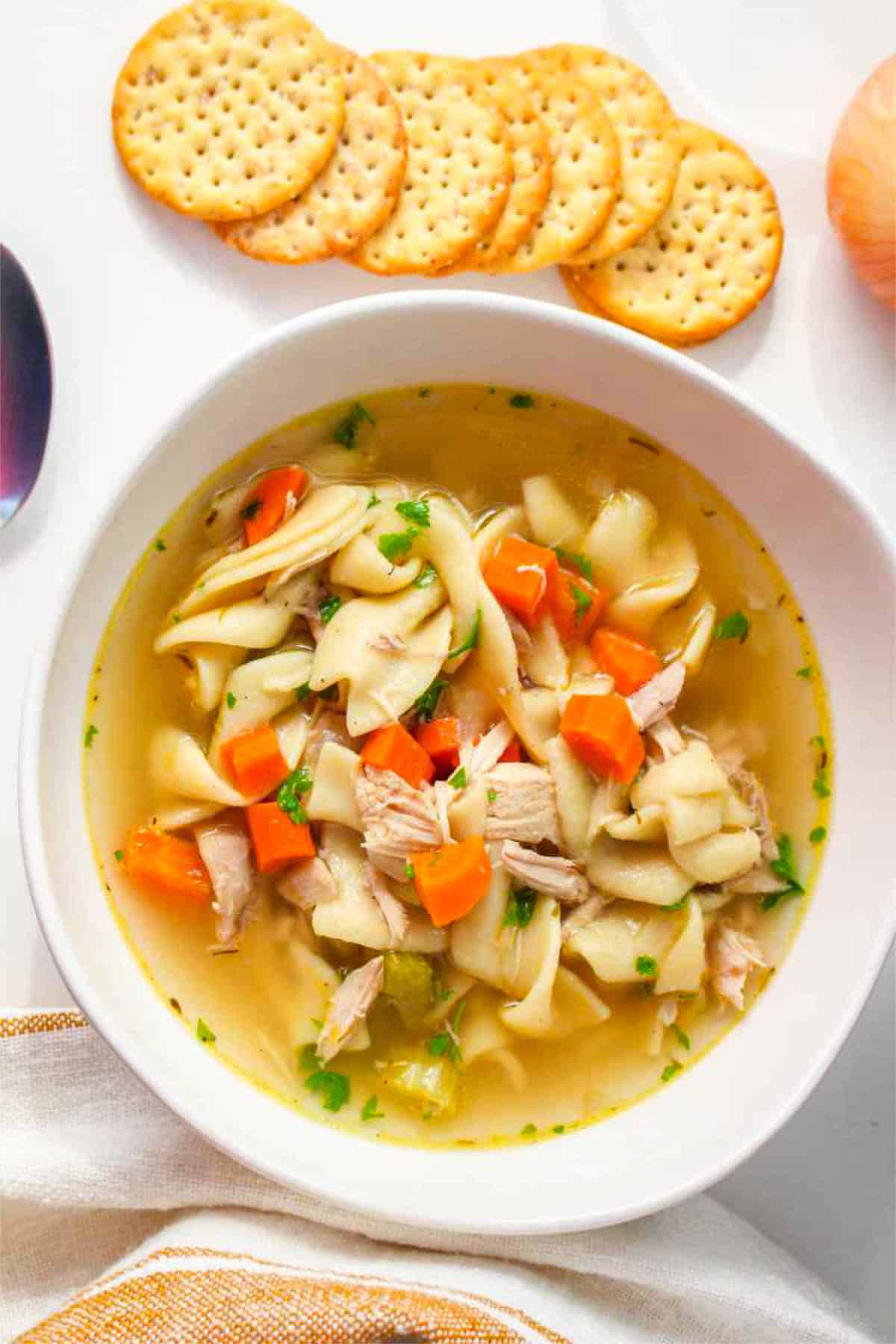 Bowl of Panera chicken noodle soup with crackers on a white surface.