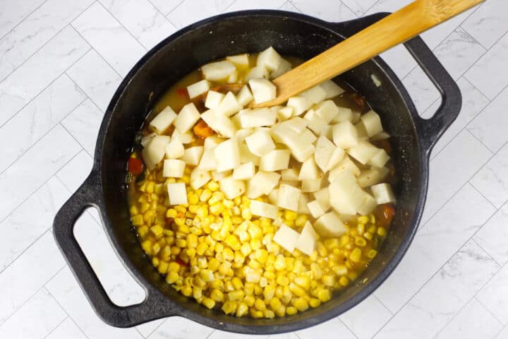 Corn, potatoes, and broth added to a pot for Panera Summer Corn Chowder.