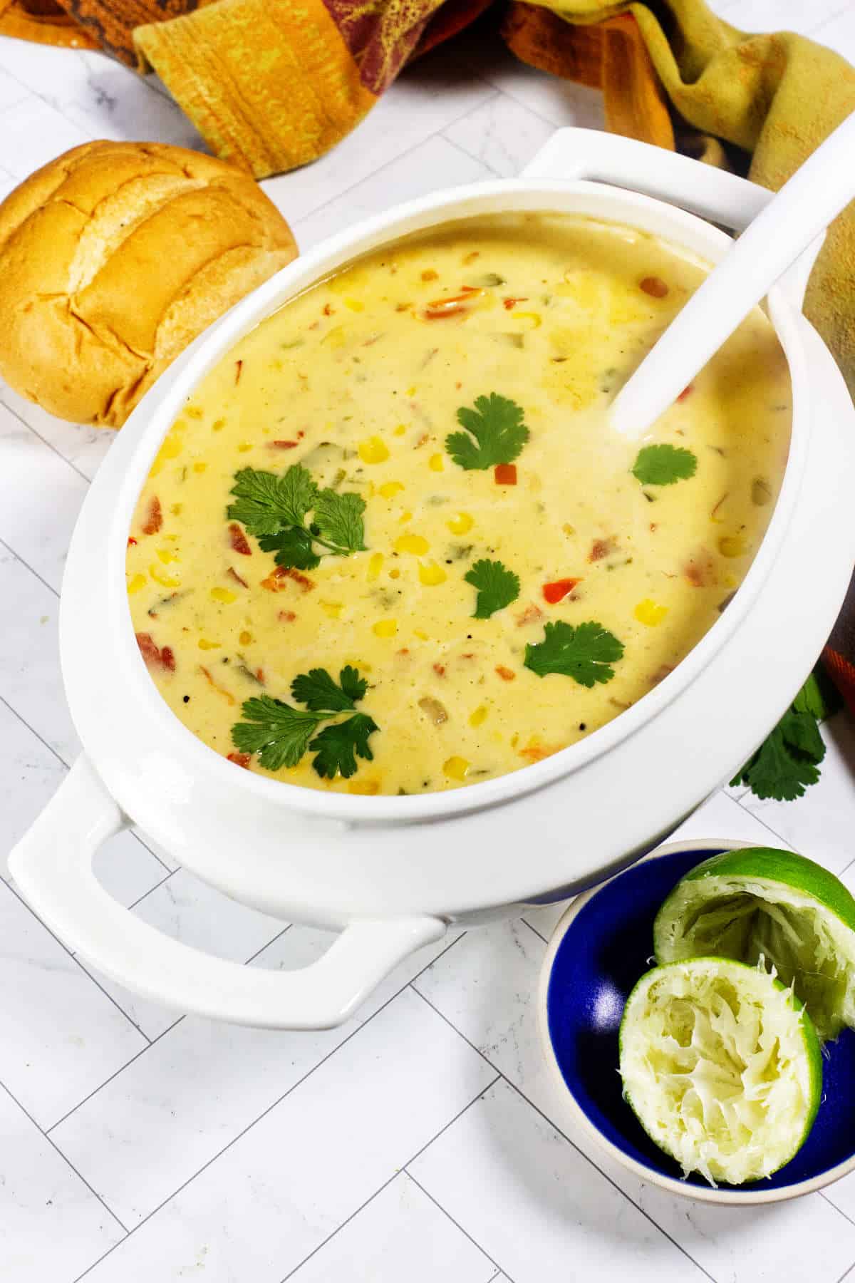 Creamy Panera Summer Corn Chowder in a blue bowl with cilantro, lime, bread roll, spoon, and colorful napkin.
