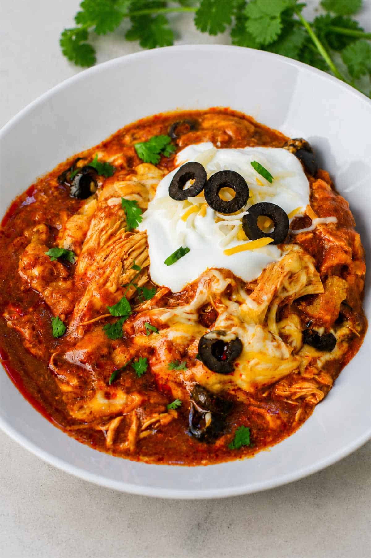 Bowl of slow cooker chicken enchilada casserole topped with sour cream, cheese, black olives, and cilantro.