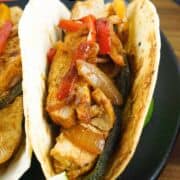 Chicken-stuffed flour tortillas with sautéed onions and peppers on a black plate, lime wedge, and "Skillet Chicken Fajitas" text.