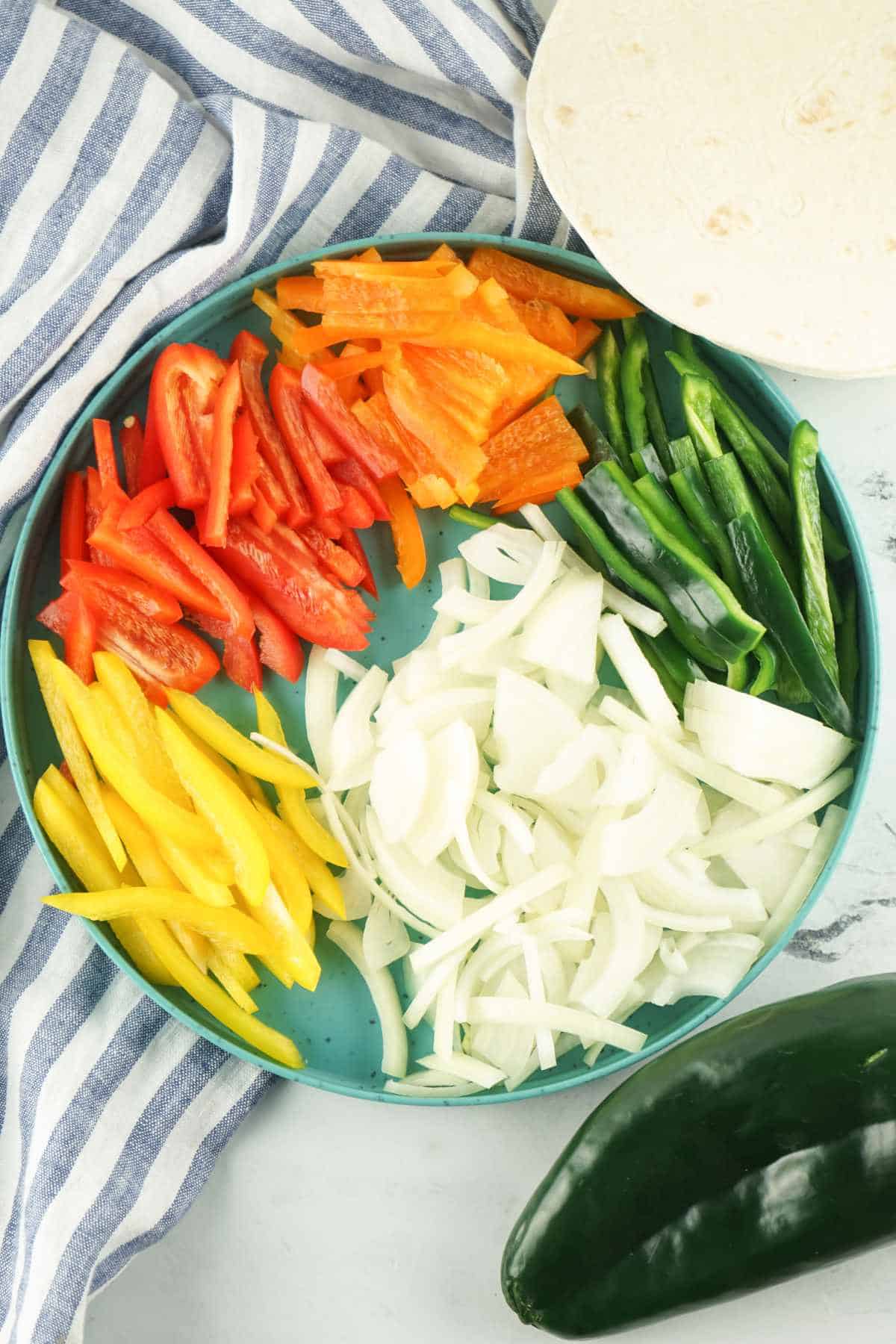 Sliced bell peppers, poblano peppers, and onions for skillet chicken fajitas.